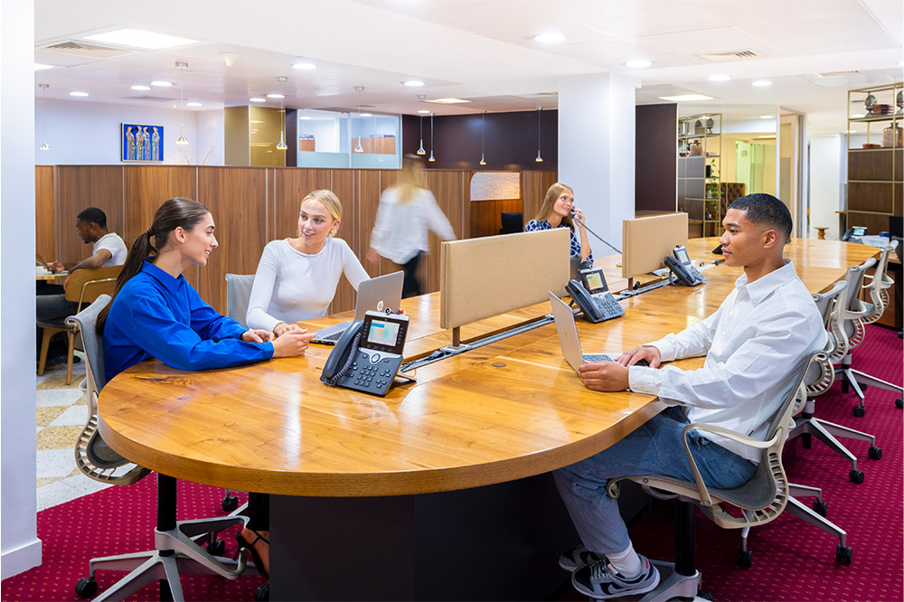 Client working and answering calls at Mayfair Coworking Space featuring a high shared desk and booths.