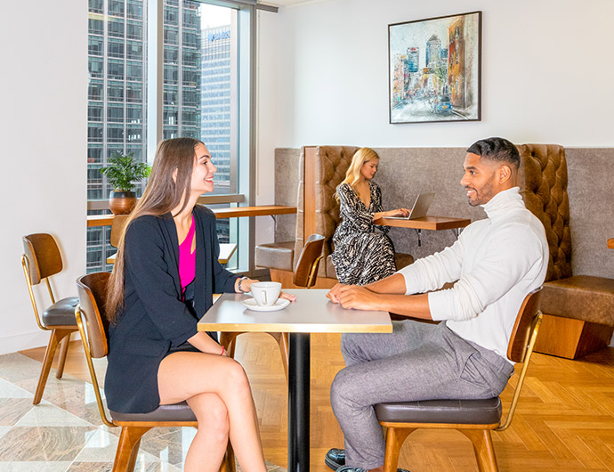 Client networking over coffee at Servcorp Canary Wharf with hot desk and collaborative booth in the background.
