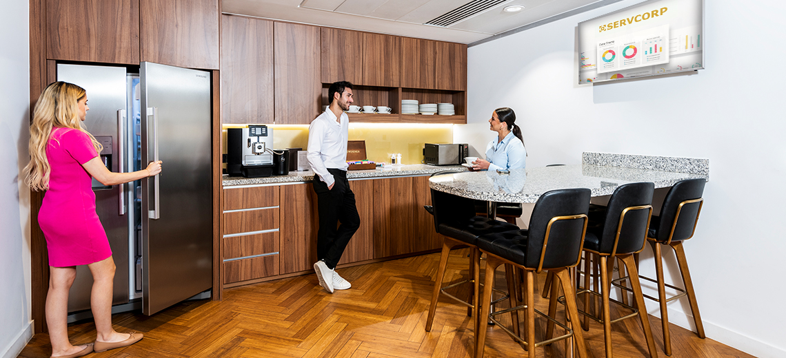 People networking and collaborating over coffee in a coworking space with a fully stocked kitchen.