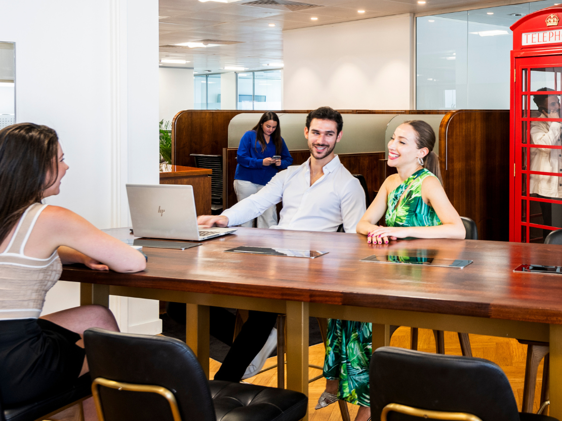 People networking and collaborating at a high table in Canary Wharf coworking space while using their phones.